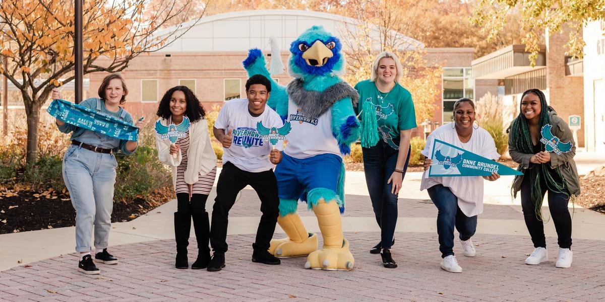 A group of students posing with AACC mascot, Swoop, while holding AACC gear.
