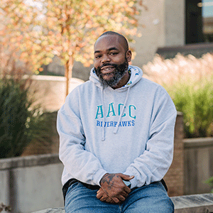 Wayne Johnson, student, sits outside on campus wearing an AACC hoodie